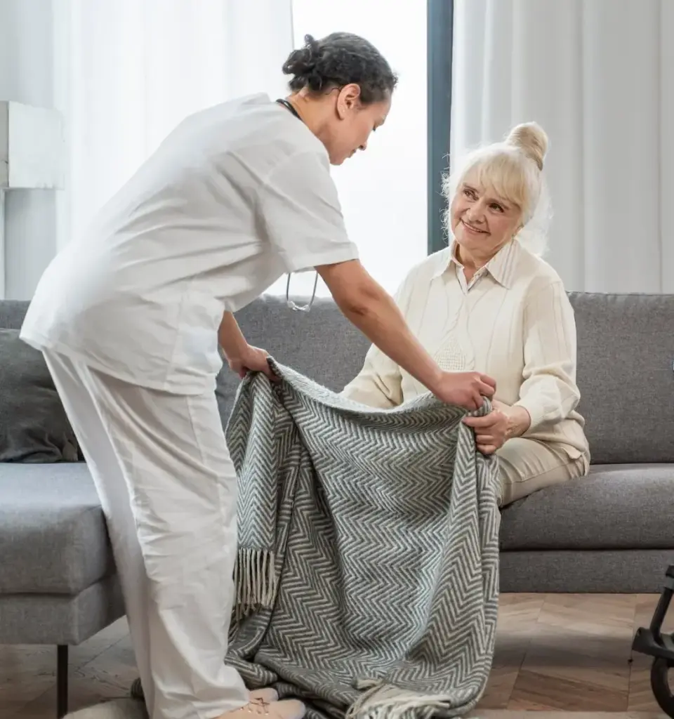 Pflegekraft legt einer Seniorin auf dem Sofa eine Decke über – fürsorgliche ambulante Betreuung und Unterstützung im Alltag für mehr Komfort und Geborgenheit zu Hause