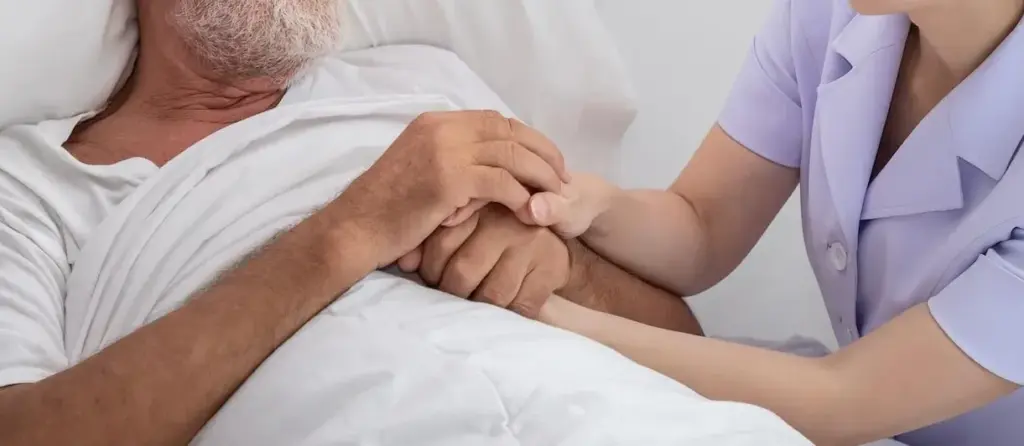 Pflegekraft hält die Hand eines älteren Mannes im Krankenbett – einfühlsame ambulante Krankenpflege und persönliche Betreuung für Sicherheit und Geborgenheit zu Hause