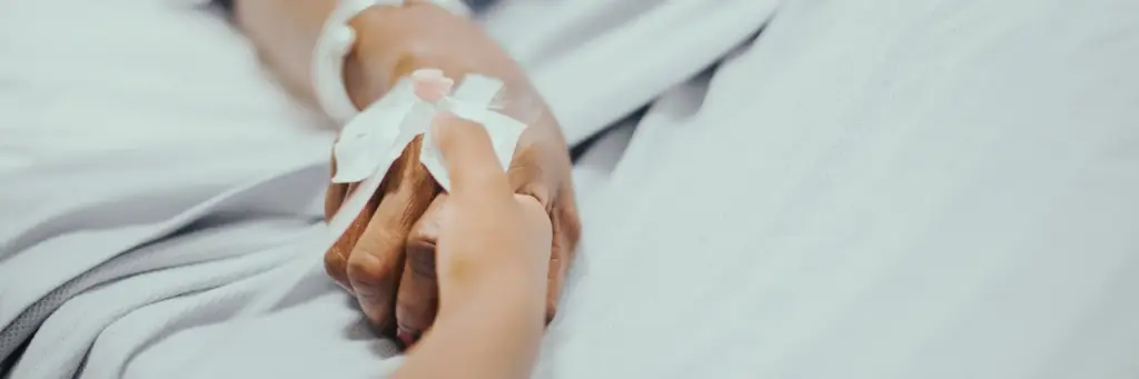 Detailaufnahme einer Hand mit Infusionszugang, die einfühlsam gehalten wird – medizinische Behandlung und fürsorgliche Betreuung durch ambulante Krankenpflege im häuslichen Umfeld